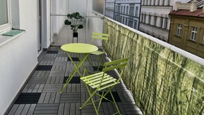 A balcony with a green table and chairs, a potted plant, and a view of buildings. - Hotel Flat in the Heart of Prague (Prague)