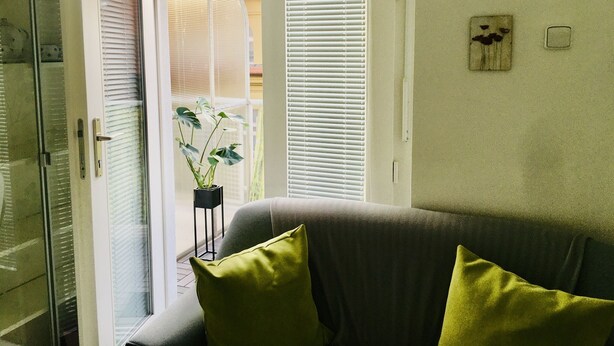 A living room with a grey sofa, green cushions, a potted plant, and a sliding glass door leading to an outdoor area. - Hotel Flat in the Heart of Prague (Prague)