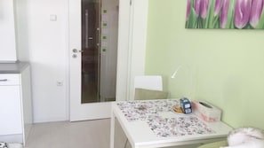 A small room with a white desk, a chair, a lamp, and a painting of tulips on the wall.