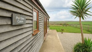 Uma cabana de madeira com a inscrição 'Pol Glas Cabin', com um caminho de concreto que leva a um campo gramado.