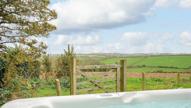A hot tub with a wooden gate labeled "PRIVATE" in a rural setting with a view of green fields and a cloudy sky.