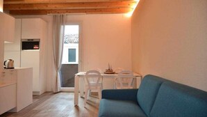 Ett kompakt bostadsutrymme med ett litet kök, en matplats med bord och stolar samt en blå soffa.