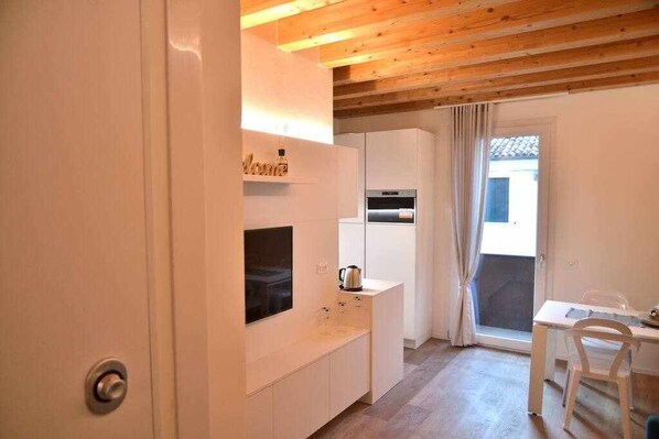 A modern kitchen with white cabinetry, a built-in oven, and a small dining area with a table and chairs.