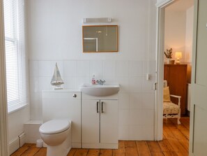 A bathroom with a toilet, sink, and cabinet. There is a window with blinds, a small sailboat decoration, and a mirror on the wall. - Shipwrights Cottage (Teignmouth)