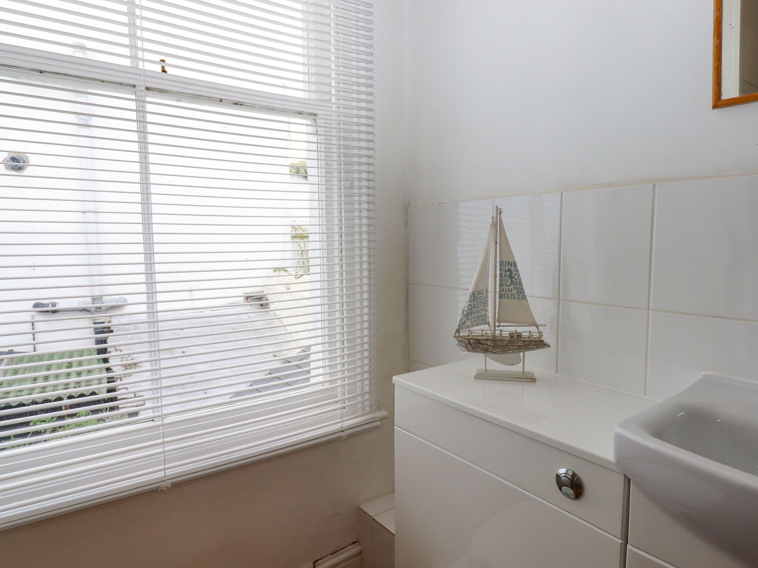 Un baño con ventana, lavabo y un modelo decorativo de velero en la encimera.