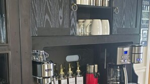 Een donkere houten bar met een koffieapparaat, diverse flessen en mokken.