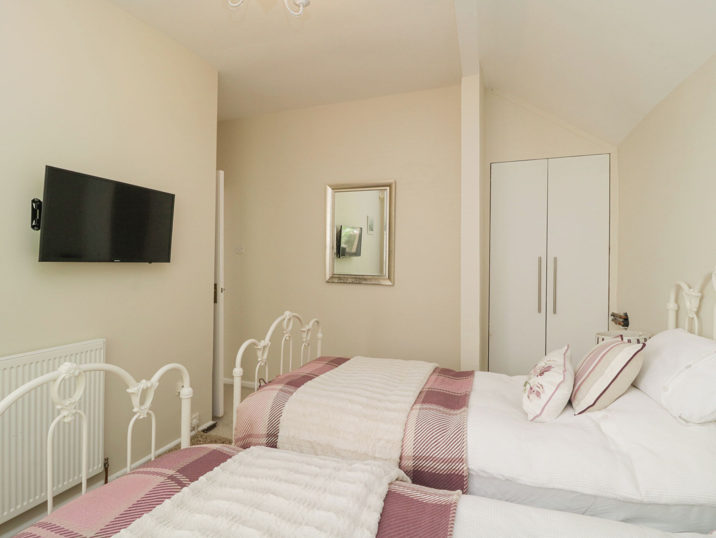 A bedroom with two beds, a TV mounted on the wall, a wardrobe, and a mirror.
