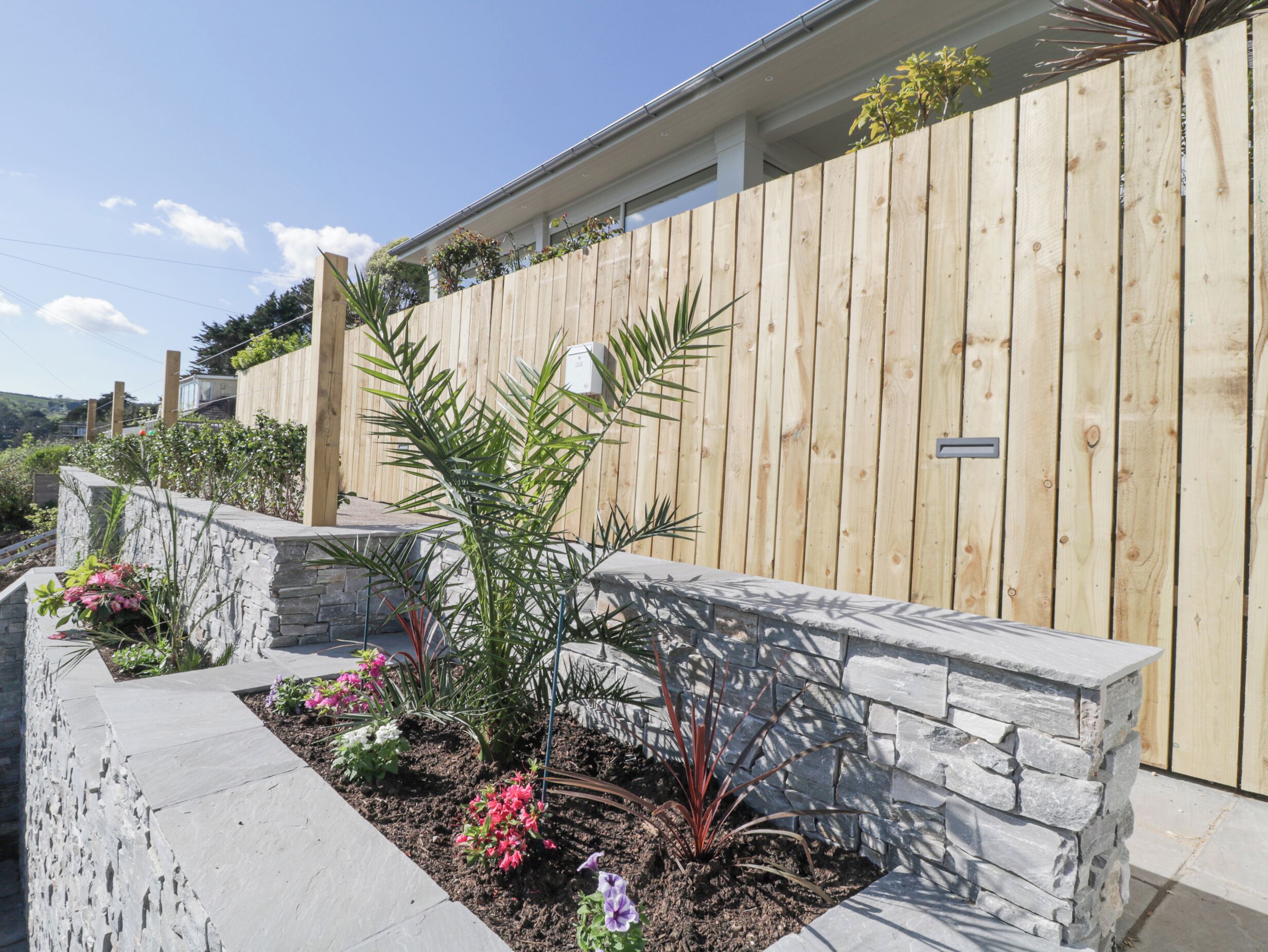 A garden with a stone wall, various plants, and a wooden fence.