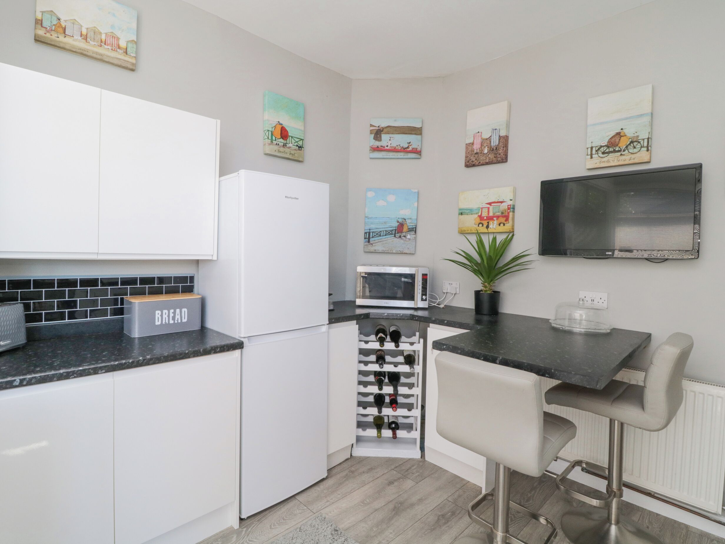 Una cocina moderna con armarios blancos, microondas integrado, estante para vinos y una zona de bar con una silla.