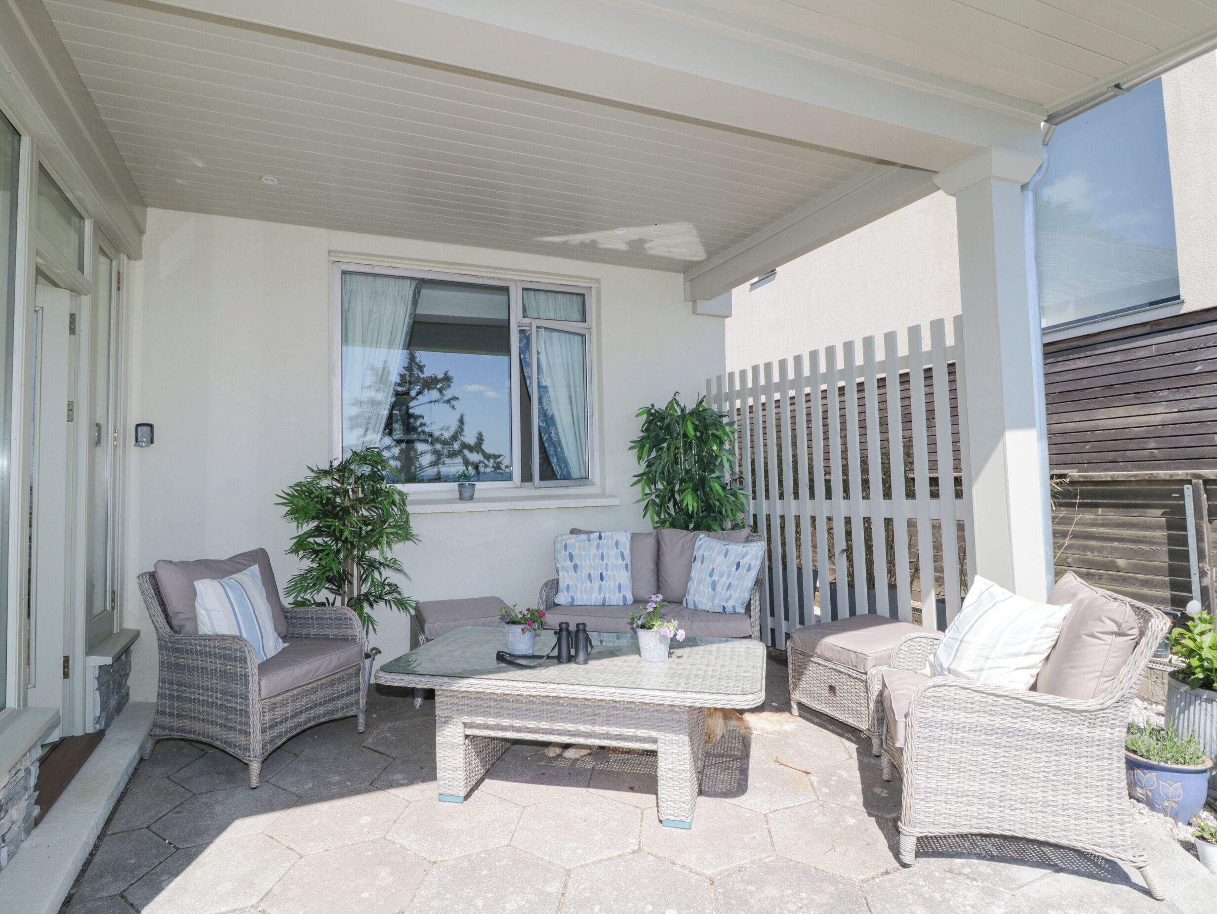 An outdoor patio with wicker furniture, a table, and potted plants.