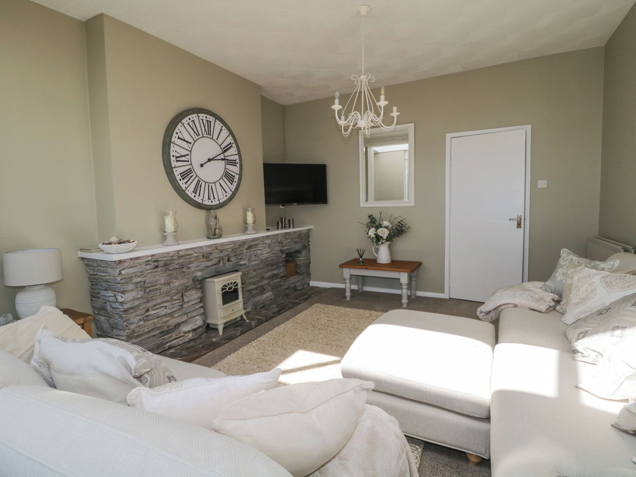 A living room with a stone fireplace, a large clock, a television, and a sofa.
