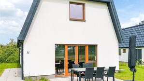 Una casa moderna de dos pisos con techo inclinado, amplios puertas correderas de vidrio y un patio con mobiliario exterior.