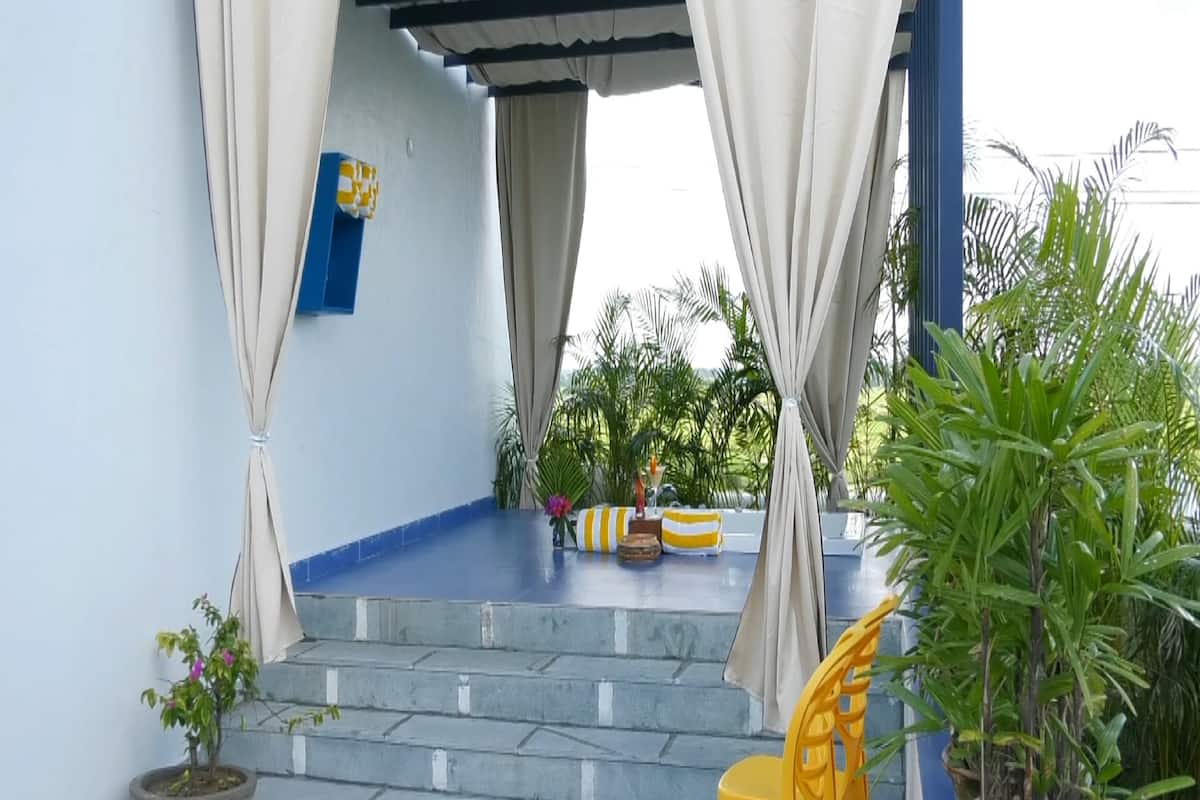 Un espace extérieur abrité, avec des marches menant à un sol recouvert de carreaux bleus, des chaises jaunes et des plantes en pot.