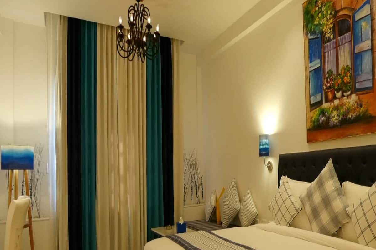 Une chambre d’hôtel avec un grand lit, un lustre, un tableau au mur et une fenêtre avec des rideaux.