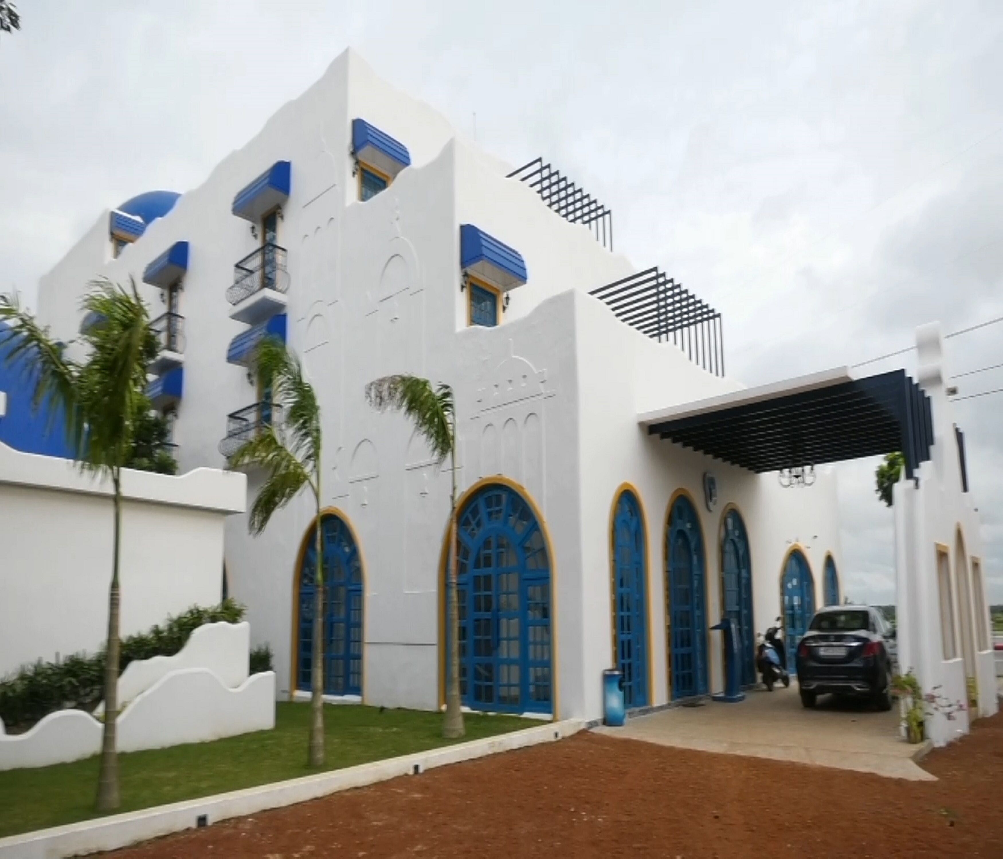 Un edificio moderno con fachada blanca y azul, amplias ventanas en arco y un acceso cubierto.