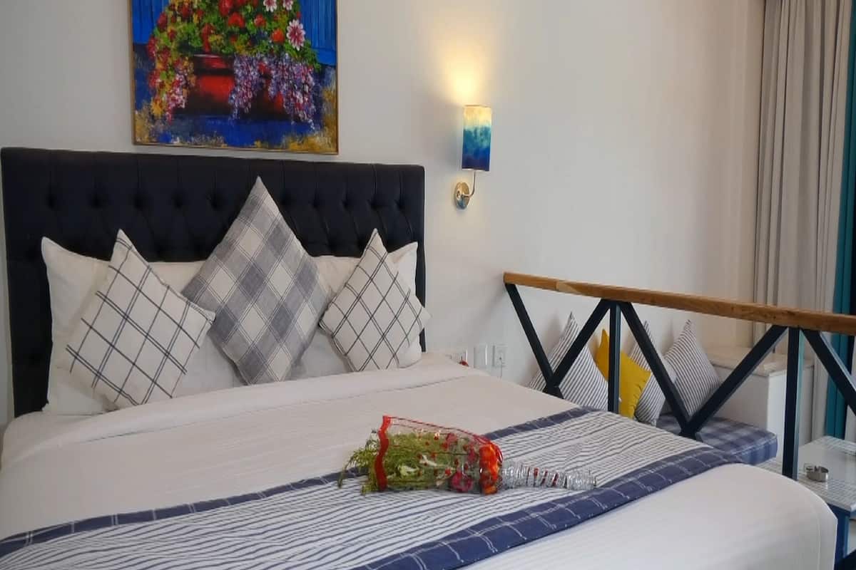 Un lit bien fait, avec une couverture à rayures, un arrangement décoratif d’oreillers, une lampe fixée au mur et un tableau au-dessus du lit.