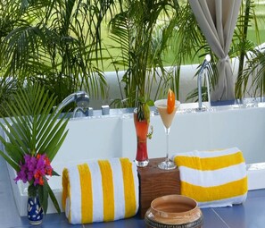 Un espace aménagé au bord de la piscine, avec une serviette à rayures, un vase rempli de fleurs, un verre à martini et un pot en terre cuite.