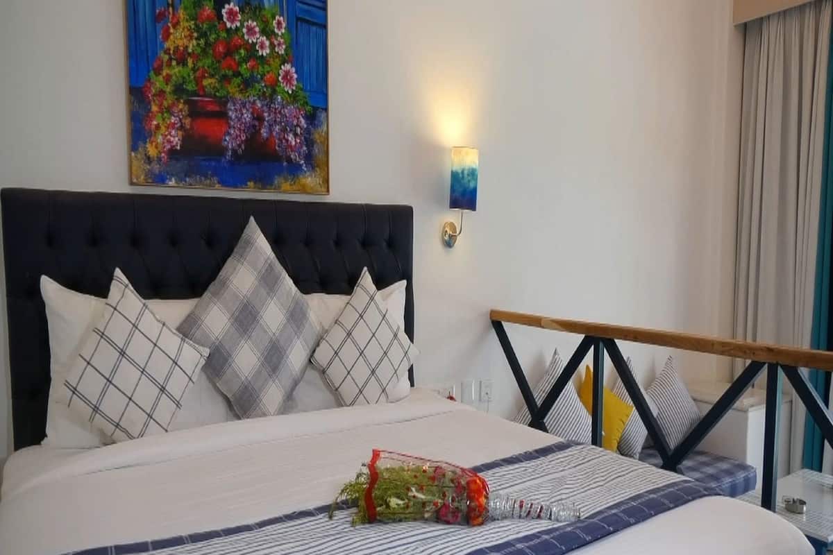 Un lit bien fait, avec une couvre-lit à rayures, un arrangement décoratif d’oreillers, un luminaire fixé au mur et un tableau au-dessus du lit.