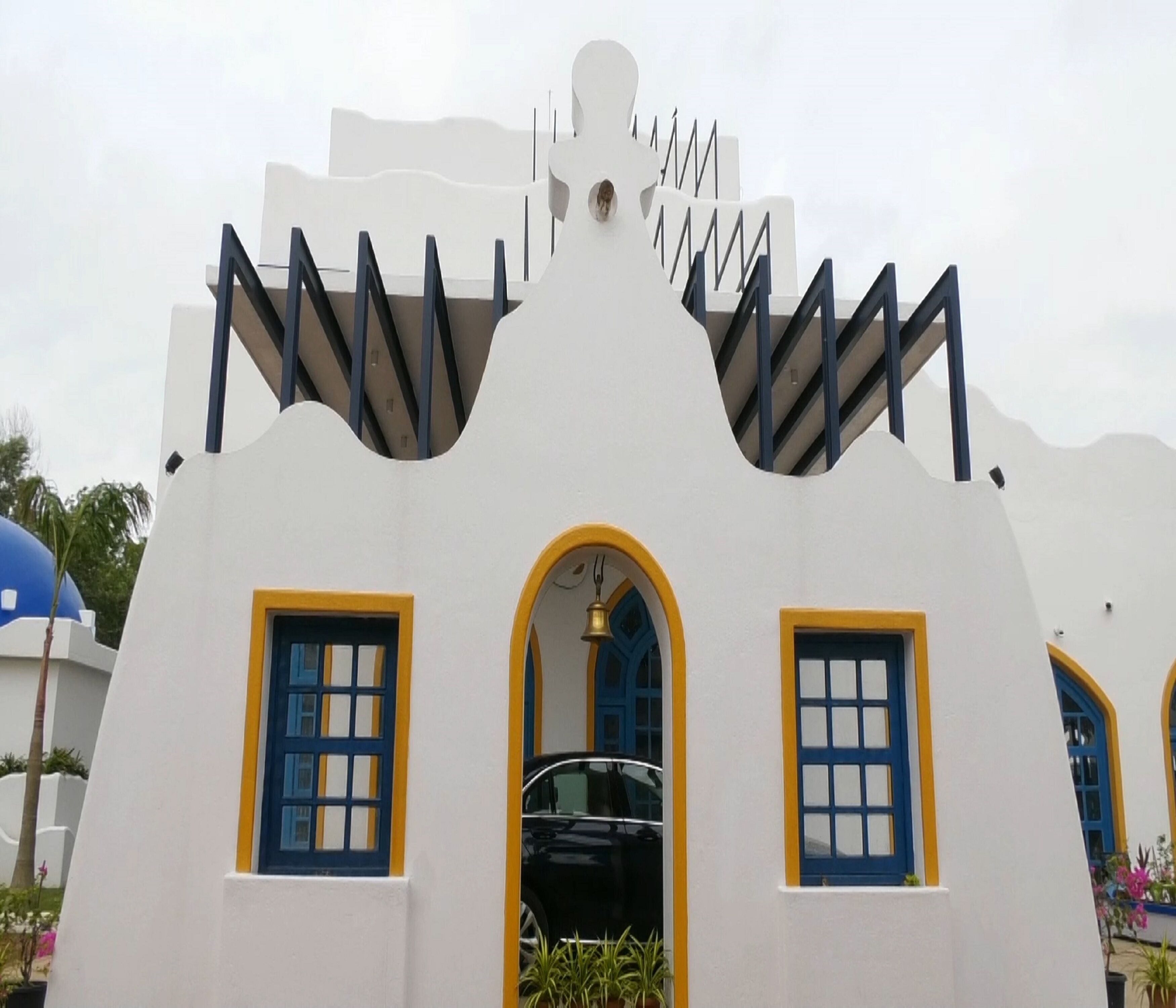 Een gebouw met een uniek architectonisch ontwerp, met een witte gevel met blauwe en gele accenten, en een zwarte auto die ervoor geparkeerd staat.