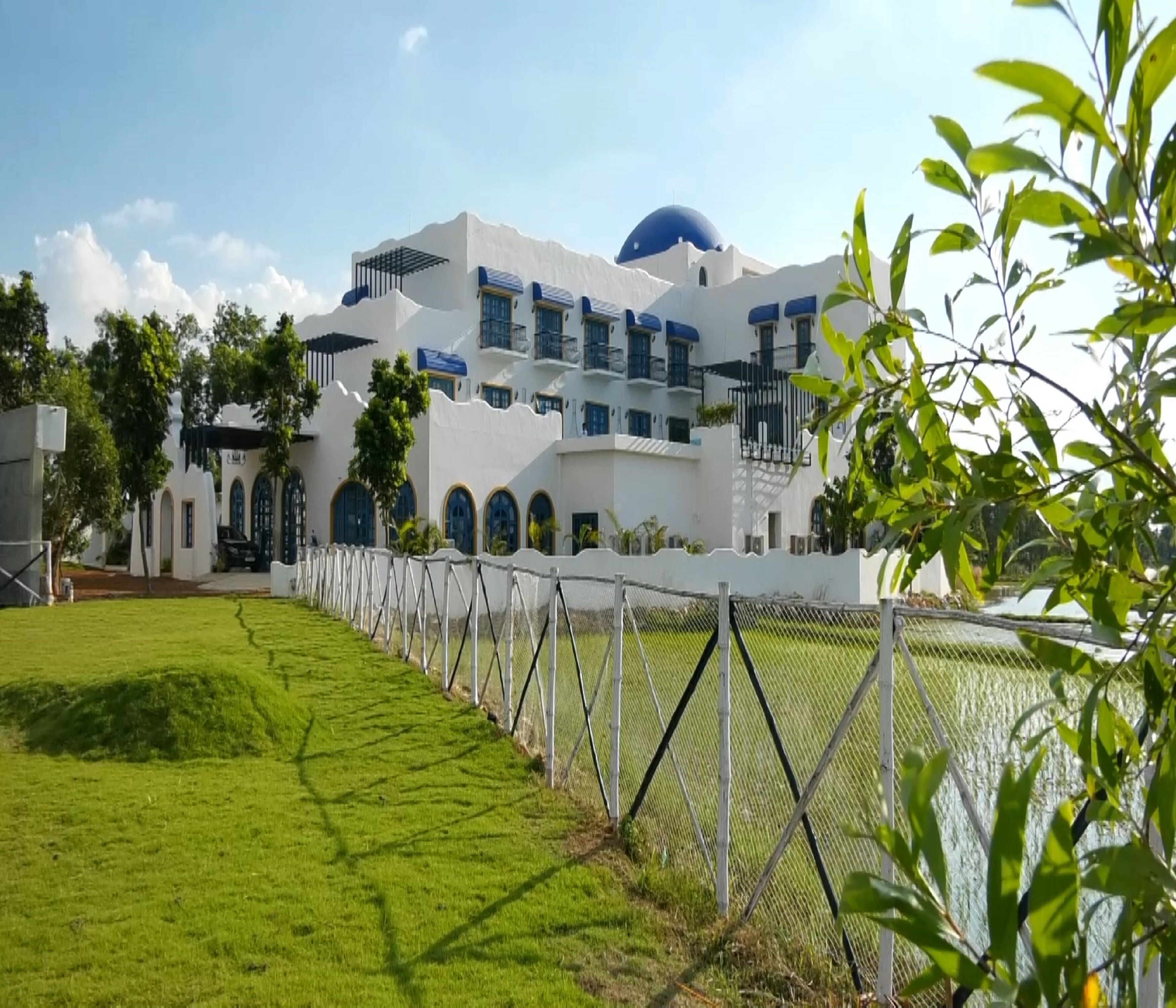 A white building with blue accents, a large dome, and a fenced garden area.