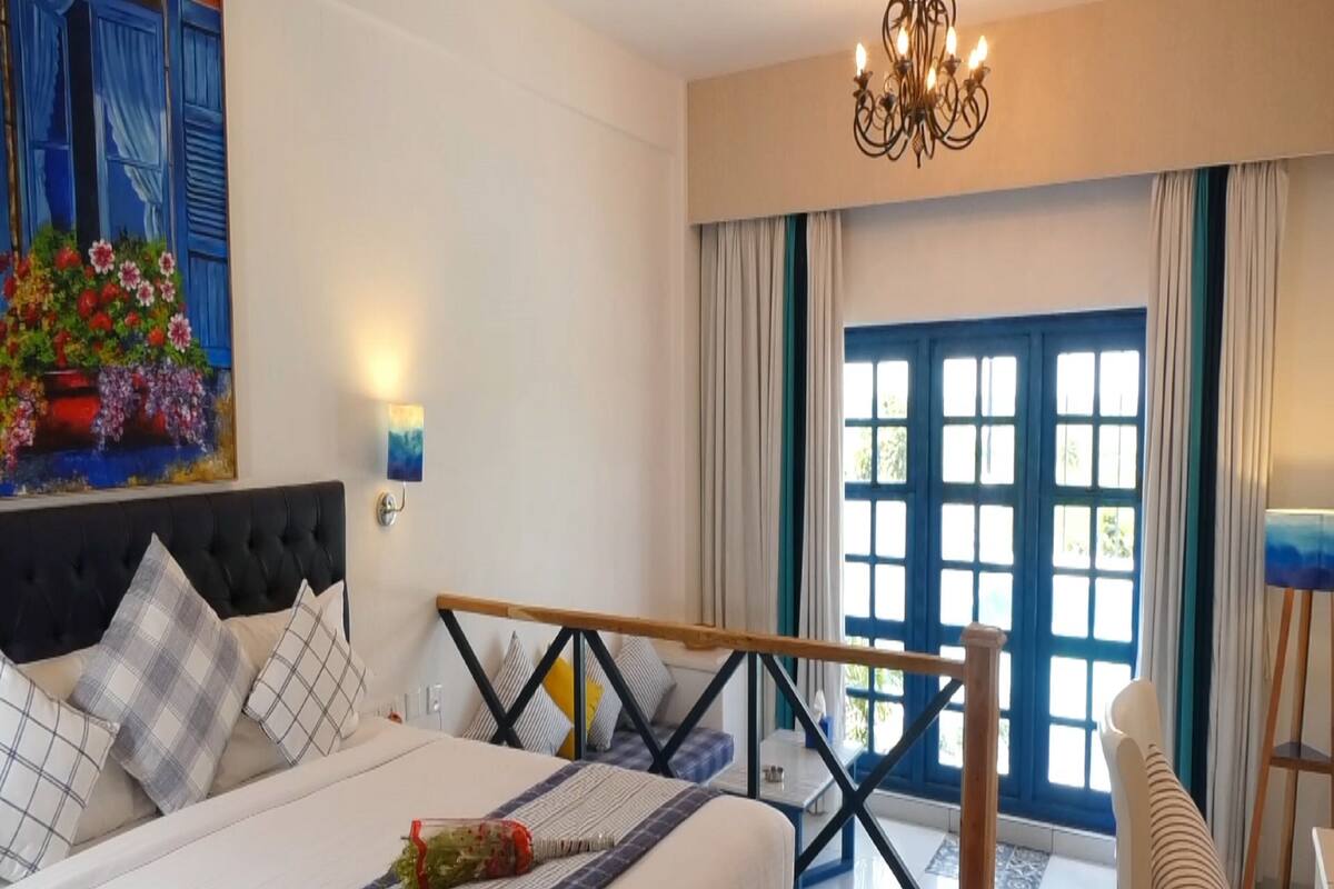 Une chambre à coucher avec un lit, un bureau, une chaise, un lustre et une fenêtre avec des rideaux.