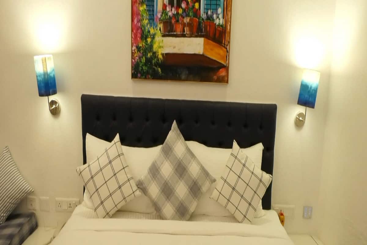 Une chambre d’hôtel avec un lit, une tête de lit, deux lampes fixées au mur et un tableau au-dessus du lit.