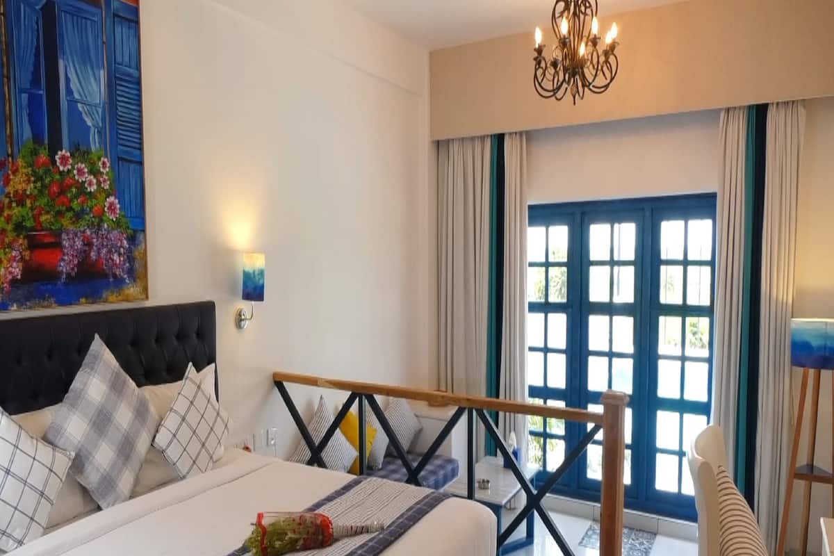 Une chambre d’hôtel moderne avec un grand lit, un banc en bois, un lustre et une vue sur l’extérieur par une porte bleue.