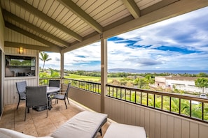A covered balcony with a dining area, a sofa, and a view of a golf course and ocean. - Wailea Ekolu 206 -Gorgeous Ocean View - AC - Close to Wailea Beach! (Kihei)