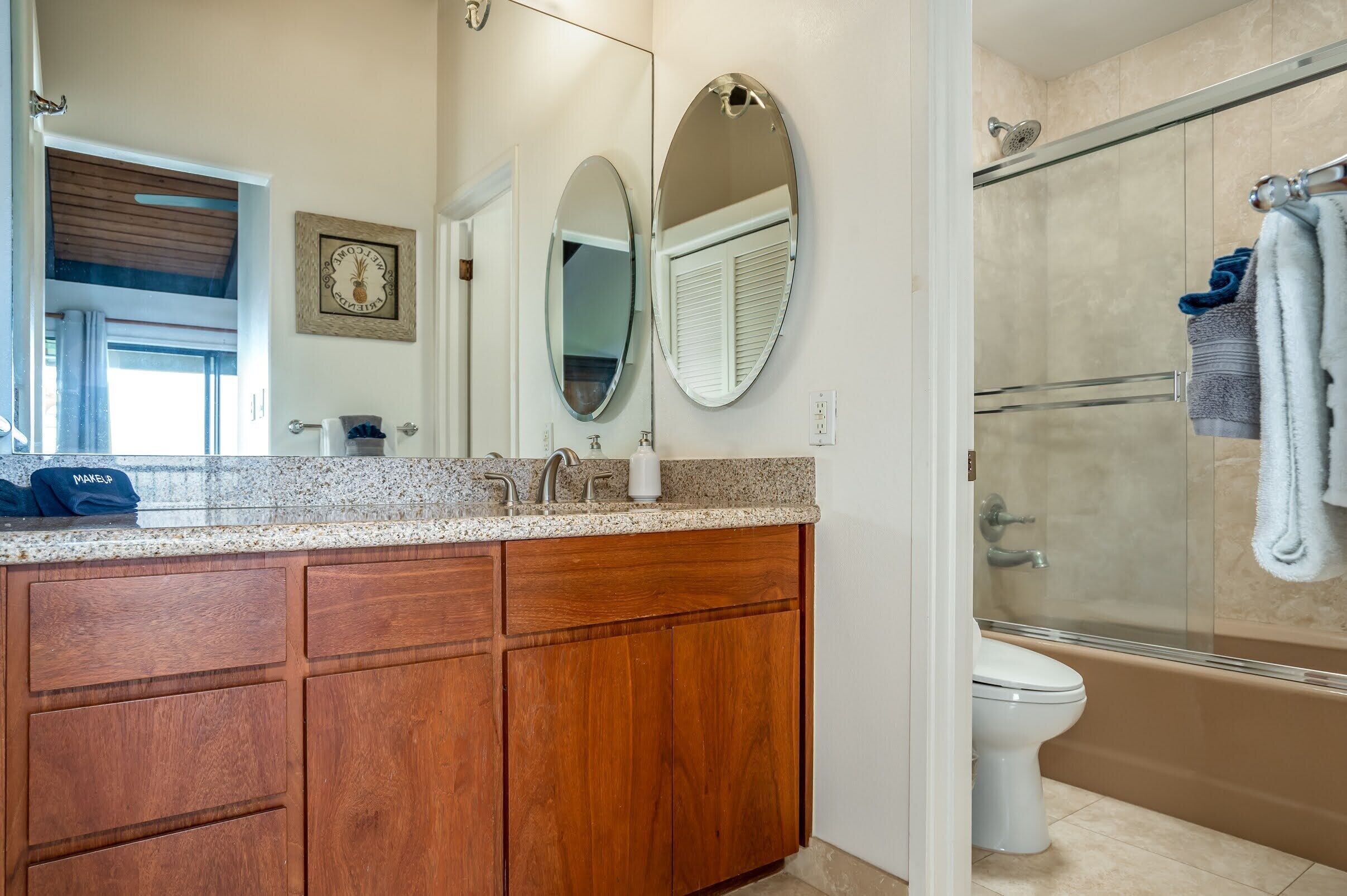 A bathroom with a wooden vanity, a double sink, a large mirror, a shower enclosure, and a toilet.