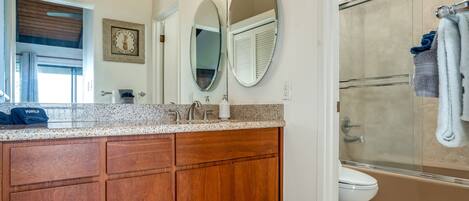 A bathroom with a wooden vanity, a double sink, a large mirror, a shower enclosure, and a toilet.