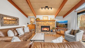 A cozy living room with a stone fireplace, leather sofas, and a large TV. - Mountain Home near Skiing, Hiking, & More (Beech Mountain)