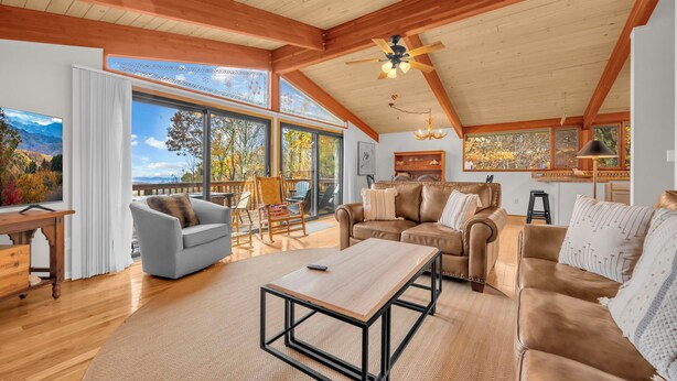 A spacious living room with wooden beams, large windows, a ceiling fan, and a view of the outdoors. - Mountain Home near Skiing, Hiking, & More (Beech Mountain)