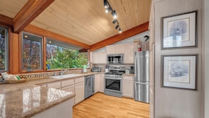 A modern kitchen with wooden beams, stainless steel appliances, and large windows overlooking a garden. - Mountain Home near Skiing, Hiking, & More (Beech Mountain)