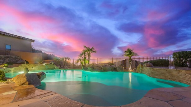 A swimming pool with a stone deck, surrounded by a fence and palm trees, under a colorful sky. - Peace in Las Sendas W/ Heated Pool/Spa! 30 night min. (Mesa)