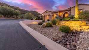 A residential house with a stone facade, a well-maintained garden with various plants and rocks, and a driveway leading to the garage. - Peace in Las Sendas W/ Heated Pool/Spa! 30 night min. (Mesa)