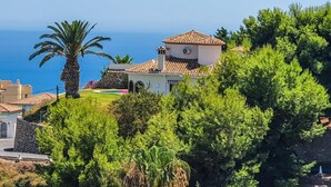 Ein Küstenhaus mit Ziegeldach, umgeben von üppiger Vegetation und Blick auf das Meer.
