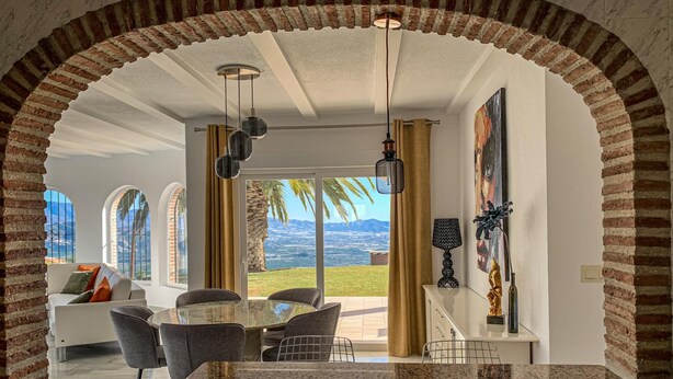 Eine moderne Küche mit einer Granit Arbeitsplatte, ein Essbereich mit einem Glastisch und ein Blick auf die Landschaft durch große Fenster.