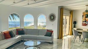 Ein geräumiges Wohnzimmer mit einem weißen Sofa, einem Glastisch und Meerblick durch große Fenster.