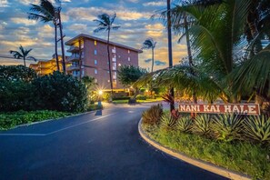 Entrada de hotel con un letrero que dice "Nani Kai Hale", rodeada de follaje tropical y palmeras.