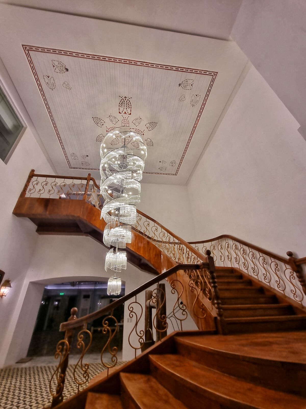 A grand staircase with a chandelier, ornate ceiling, and a view of the interior space.
