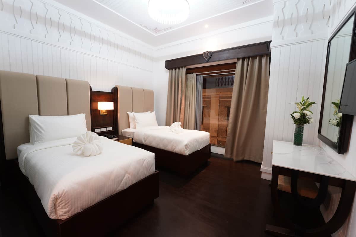 Une chambre d’hôtel avec deux lits, un bureau, une télévision et une fenêtre avec des rideaux.