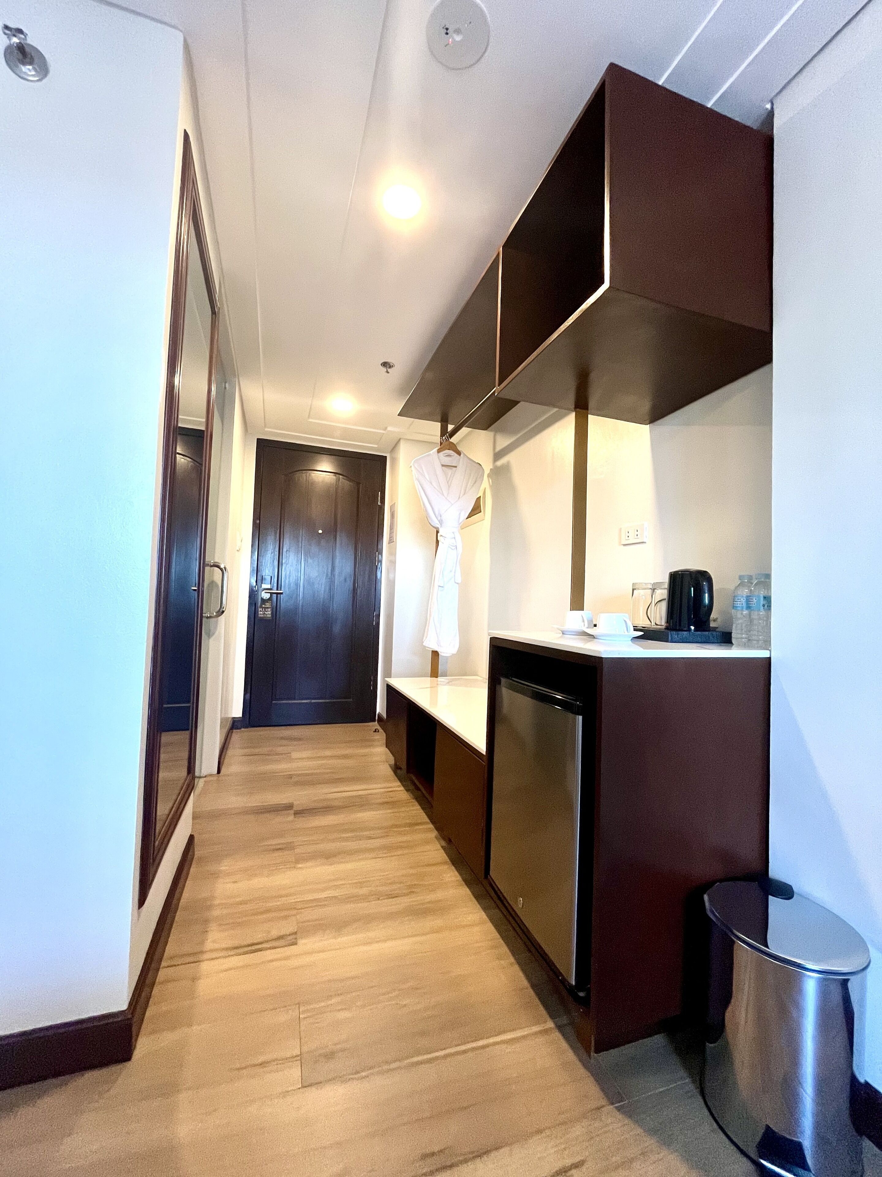 Una habitación de hotel compacta con kitchenette, un pequeño cubo de basura y una bata colgada en la pared.