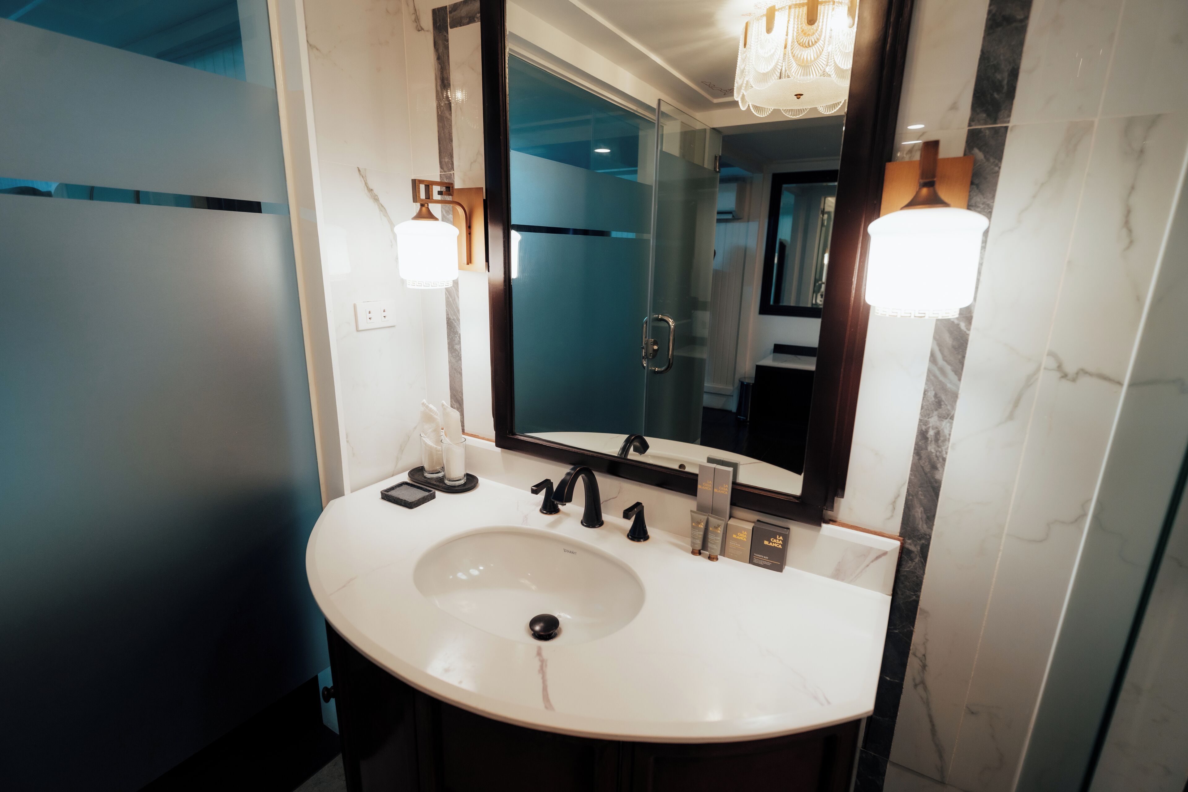 A modern bathroom with a large mirror, a white sink, and two wall-mounted lights.