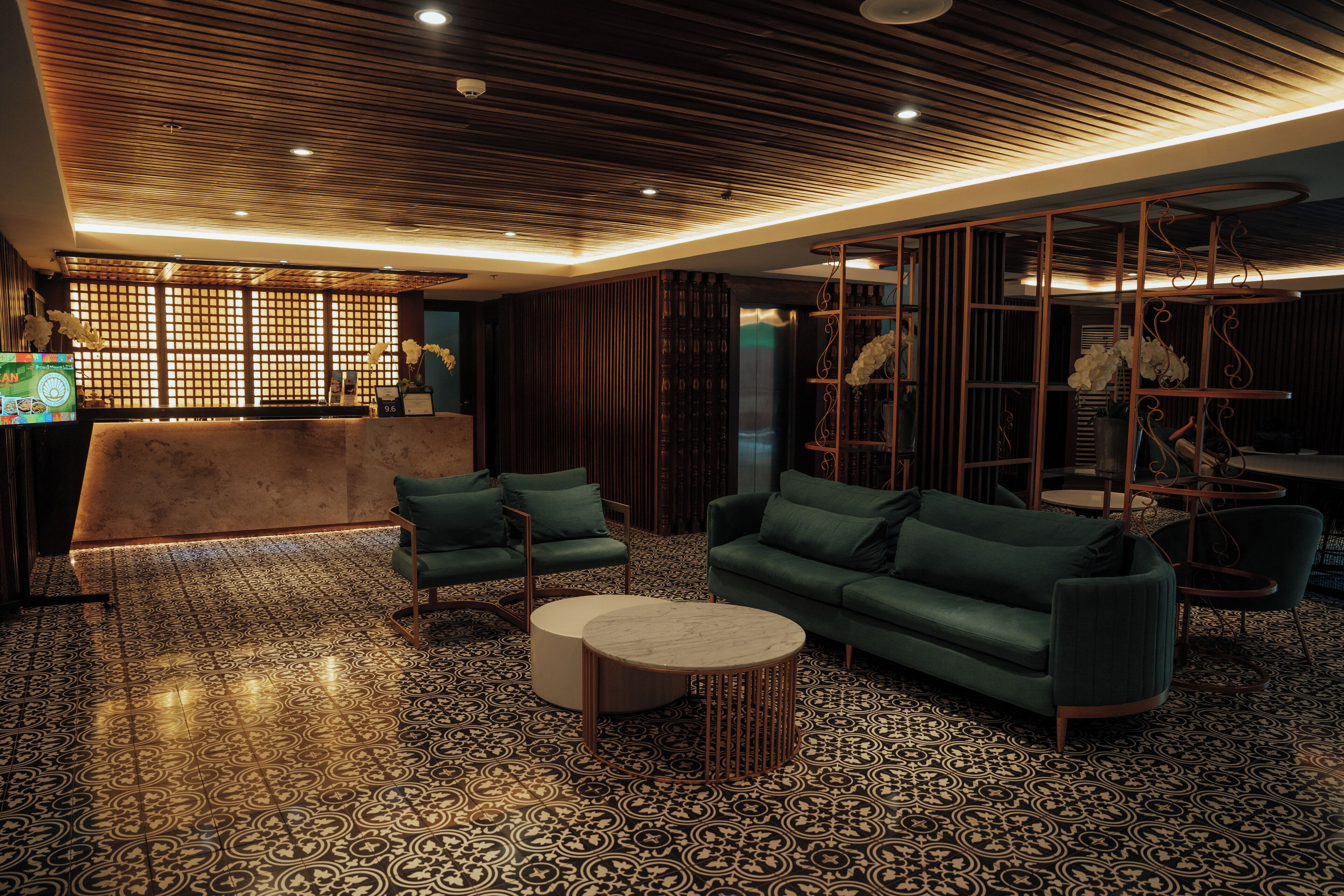 Eine moderne Lobby mit einem gemusterten Boden, grünen Sofas, einem runden Couchtisch und einer Rezeption mit einer Holzwand.