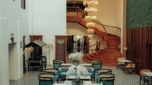 A spacious lobby with a geometric patterned floor, teal seating, a central table, and a staircase leading to an upper level. - La Casa Blanca de Vigan Hotel (Vigan)