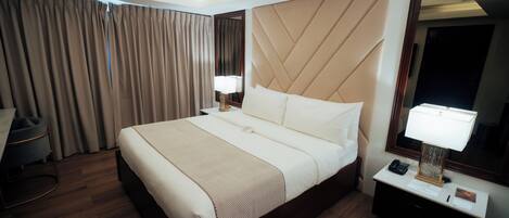 A hotel room with a large bed, a desk with a chair, a desk lamp, a telephone, and a mirror.