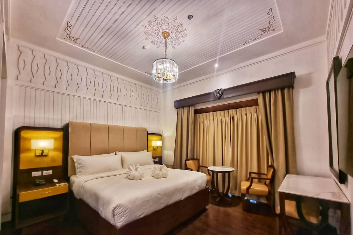 Une chambre d’hôtel avec un grand lit, deux lampes de chevet, un lustre, une petite table et une chaise.