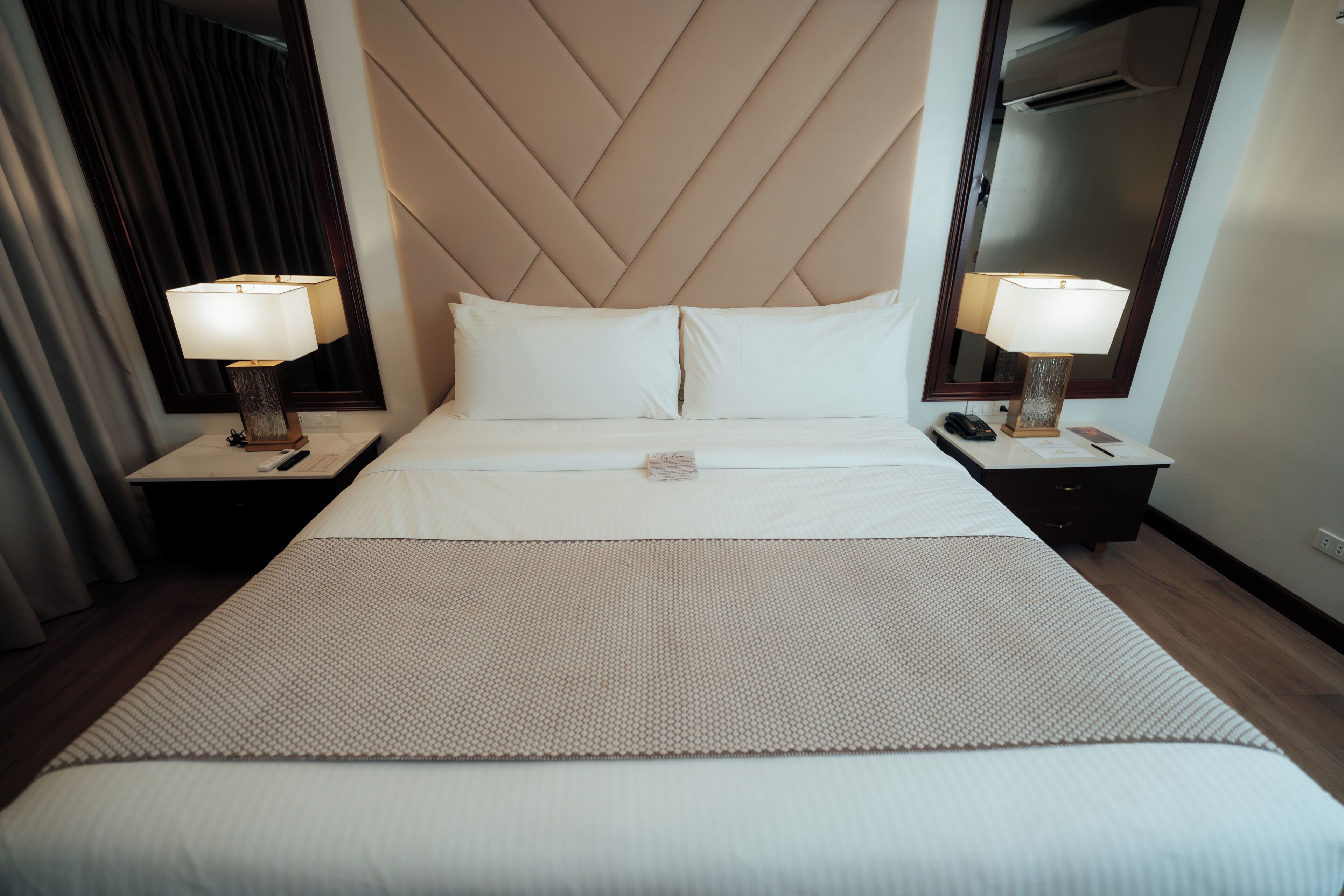 A hotel room with a large bed, two bedside tables with lamps, a mirror, and a wooden headboard.