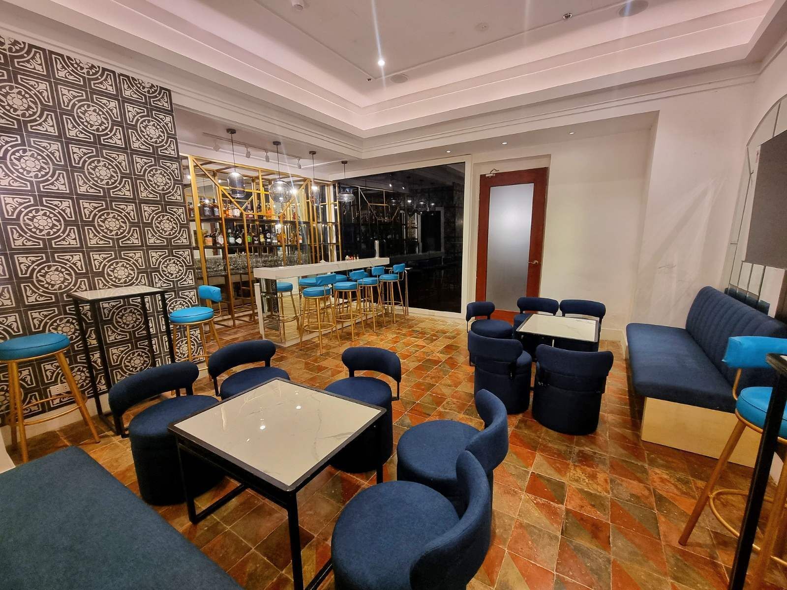 Un restaurant moderne doté d’un bar, de différents types de tables et de chaises, et d’un mur orné de motifs.