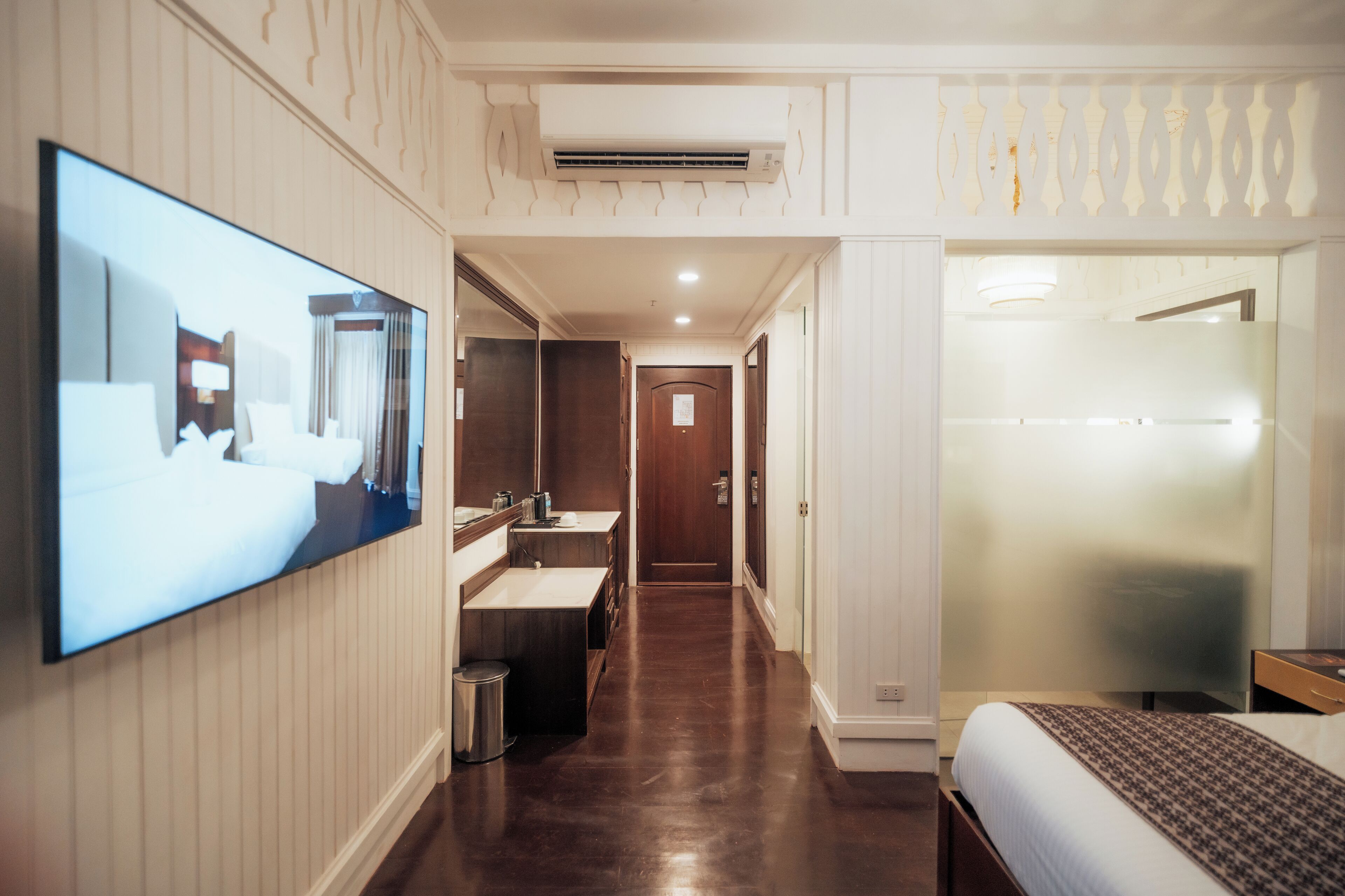 A hotel room with a large TV, a bathroom with a mirror and sink, and a bed with a patterned bedspread.
